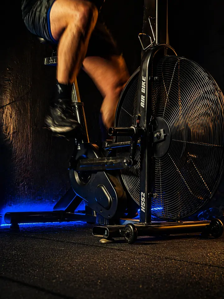 A person cycling on an air bike with a large fan