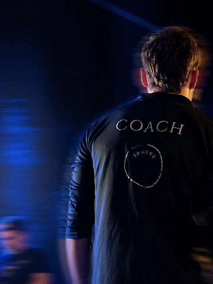 A coach wearing a black Sphere branded shirt, viewed from behind