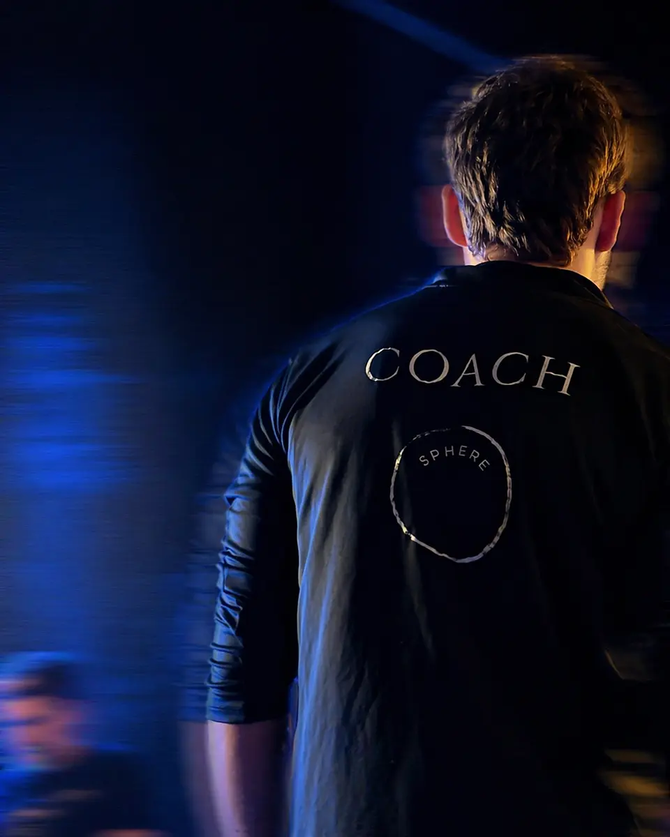 A coach wearing a black Sphere branded shirt, viewed from behind